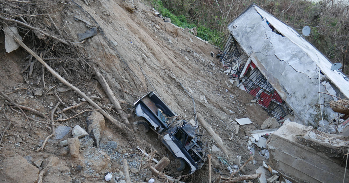 Destroyed building alongside hill with smashed truck