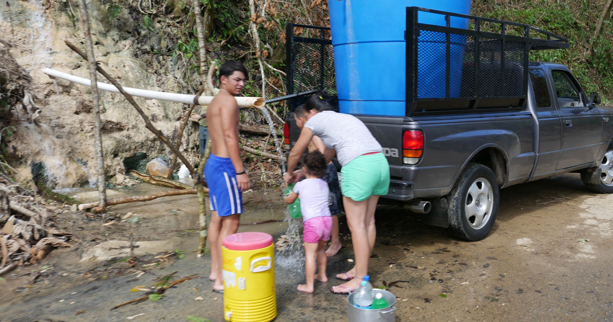 People getting water from pipe along a dirt road