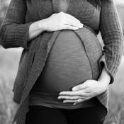 Pregnant woman stands holding her stomach - thumbnail