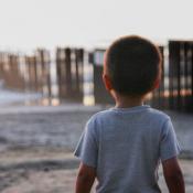 Child stares at border fence