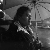 Woman looks out from under umbrella in the rain.