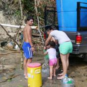 People getting water from pipe along dirt road