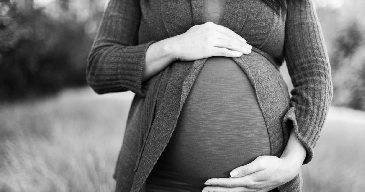 Pregnant woman stands holding her stomach