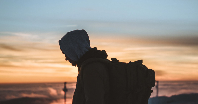 A person with hood and backpack walks at sunset