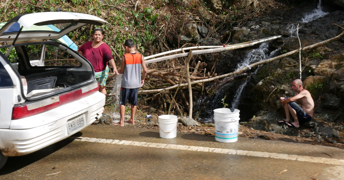 People filling containers with water from small waterfall