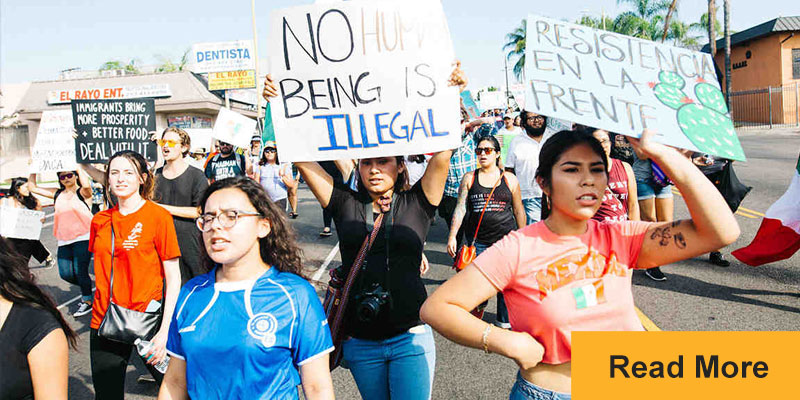 People marching in street one sign reads "No Human Being is Illegal"